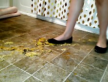 Suzi walks over unpeeled bananas,  on floor,  wearing her black ballet flats