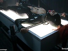 Ginger black serf Daisy Ducati in latex costume shacled laid on illuminating table and snatch bibed then clamped and booty hooke