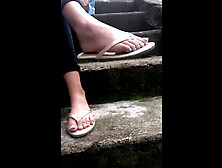 Amateur girl shows her sexy feet with blue toe nails in her flip-flops while sitting on the stairs