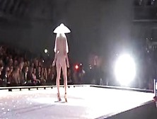 Seductive fashion model in a weird hat walks down the catwalk in the nude